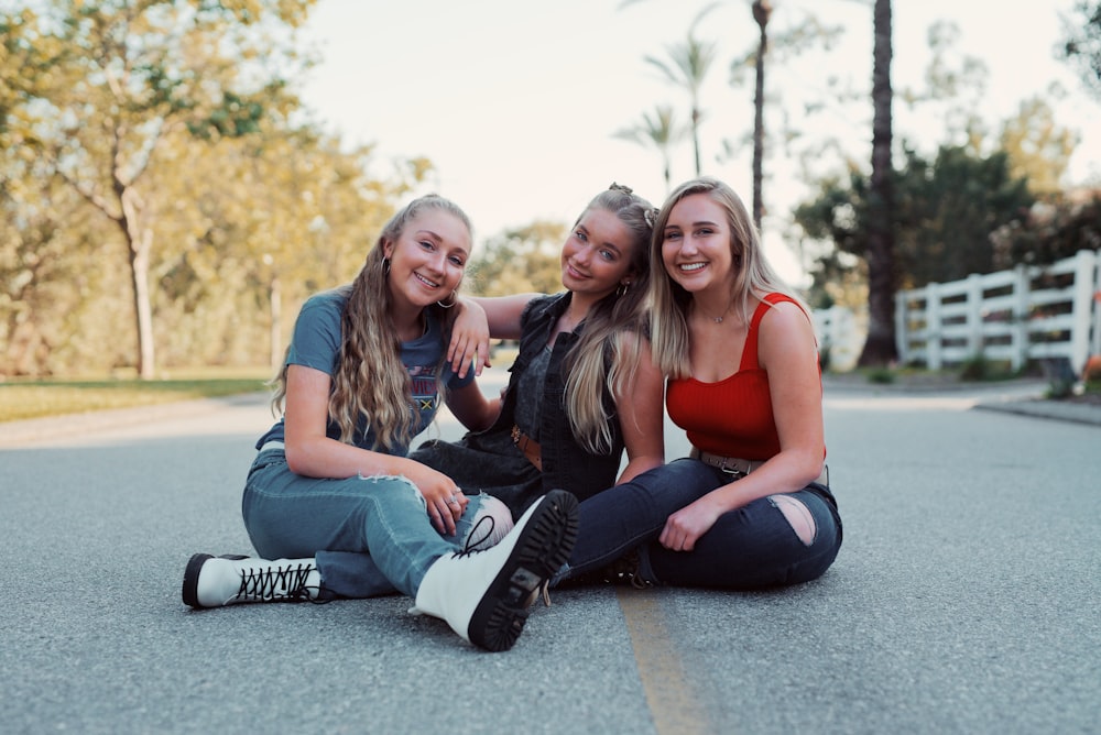 3 women sitting on gray concrete floor during daytime