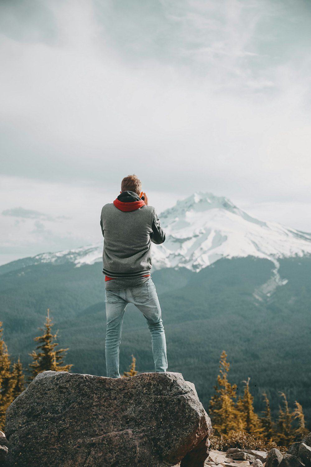 man in gray jacket and gray pants holding black dslr camera standing on brown grass field