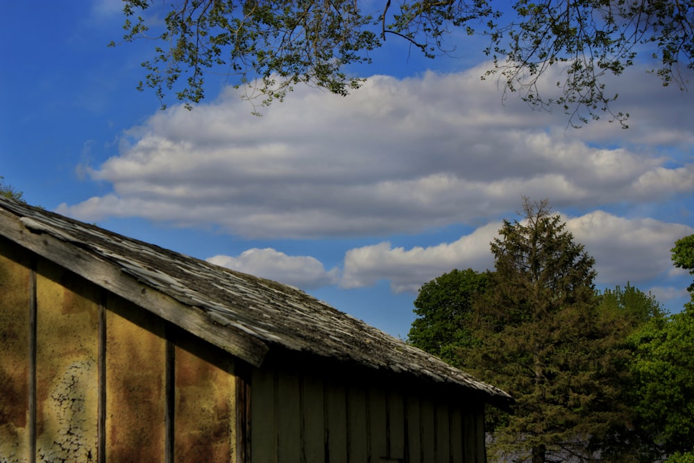 brown wooden house near green tree under white clouds and blue sky during daytime