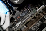 A close-up view of a computer motherboard featuring an ASUS label. A NVMe M.2 SSD labeled Samsung 970 EVO Plus is prominently installed. Various other components, such as cables, a cooling unit, and GPU with EVGA branding, are visible.