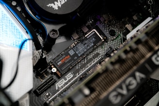 A close-up view of a computer motherboard featuring an ASUS label. A NVMe M.2 SSD labeled Samsung 970 EVO Plus is prominently installed. Various other components, such as cables, a cooling unit, and GPU with EVGA branding, are visible.