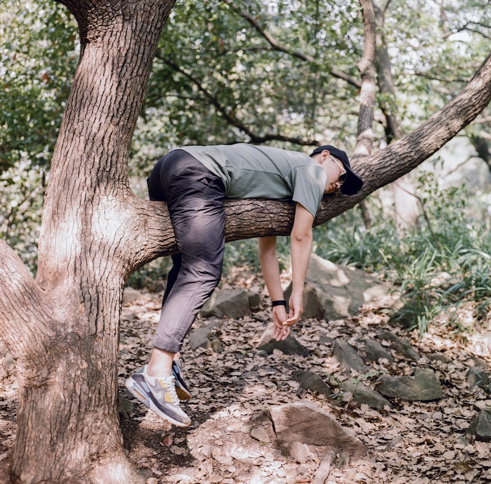 man in black t-shirt and blue denim jeans sitting on tree branch