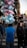 A person wearing a blue jacket is seen from the back, standing in a crowded street, holding a large bunch of pre-packaged cotton candy in various colors including pink, blue, and white. The street is filled with pedestrians and various storefronts are visible in the background.