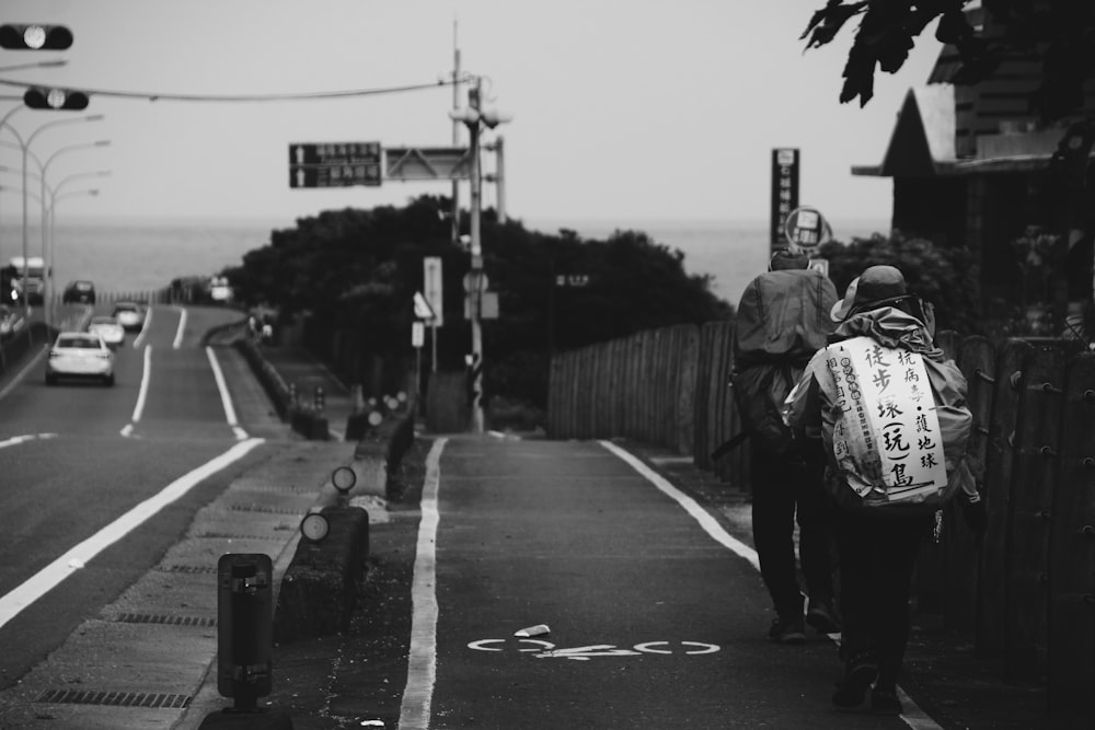 grayscale photo of man in black jacket and pants walking on street