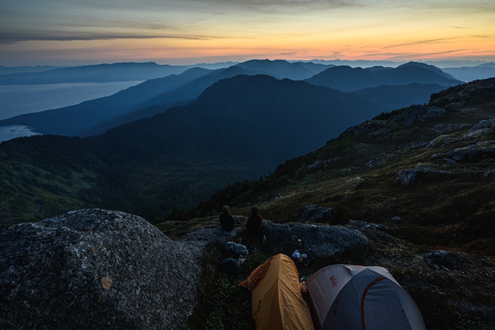 person sitting on rock near tent on top of mountain during daytime