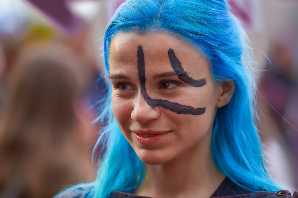 mujer con el pelo azul con pintura negra en la cara