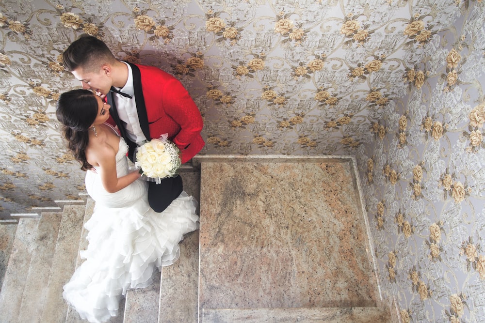 hombre en traje rojo besando a mujer en vestido de novia blanco