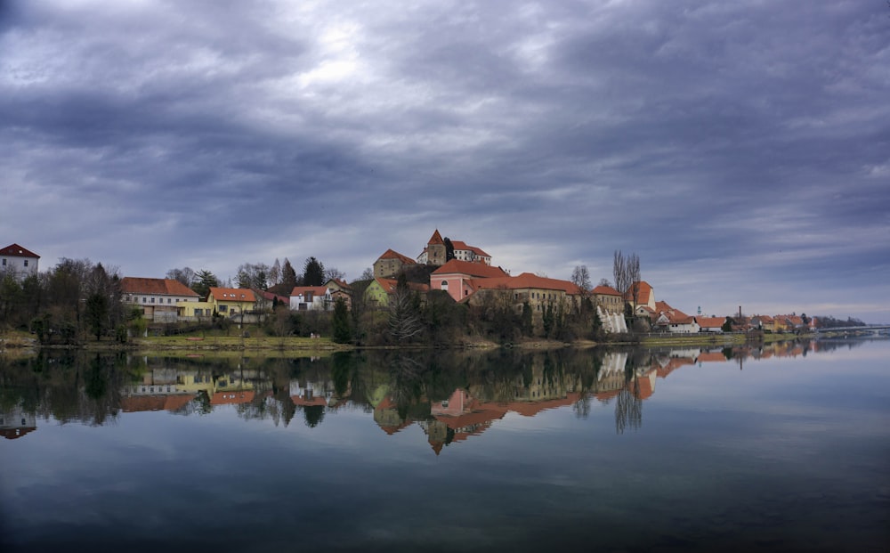 brown and white concrete house near body of water under gray clouds