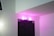 A doorway labeled as a toilet is illuminated with pink lighting, set against a white wall. The door is dark-colored with a specific geometric pattern.