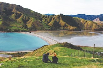 man and woman sitting on grass field near lake during daytime