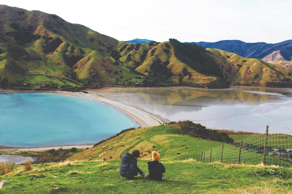 man and woman sitting on grass field near lake during daytime