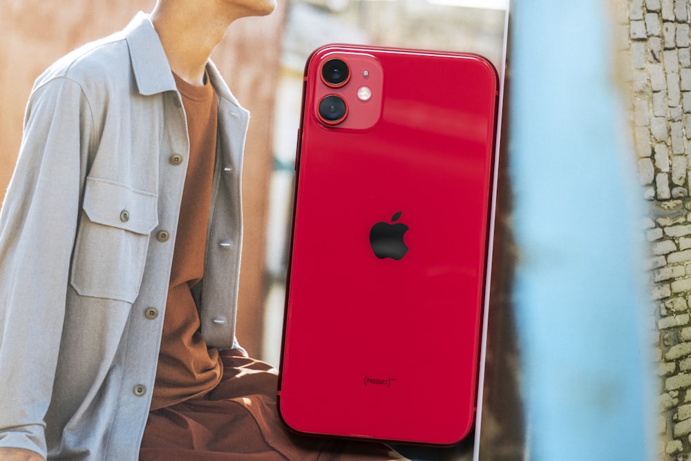 Hombre con camisa abotonada marrón sosteniendo un iPhone 7 Plus rojo