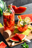 Bright pink watermelon and lemon juice with ice cubes and lemon wedges on the side.