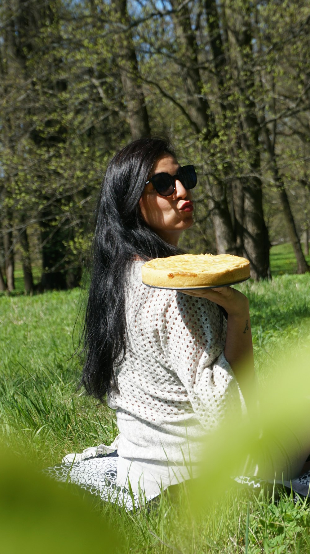 Mujer con camisa de punto blanca y gafas de sol negras sosteniendo una bandeja de madera marrón