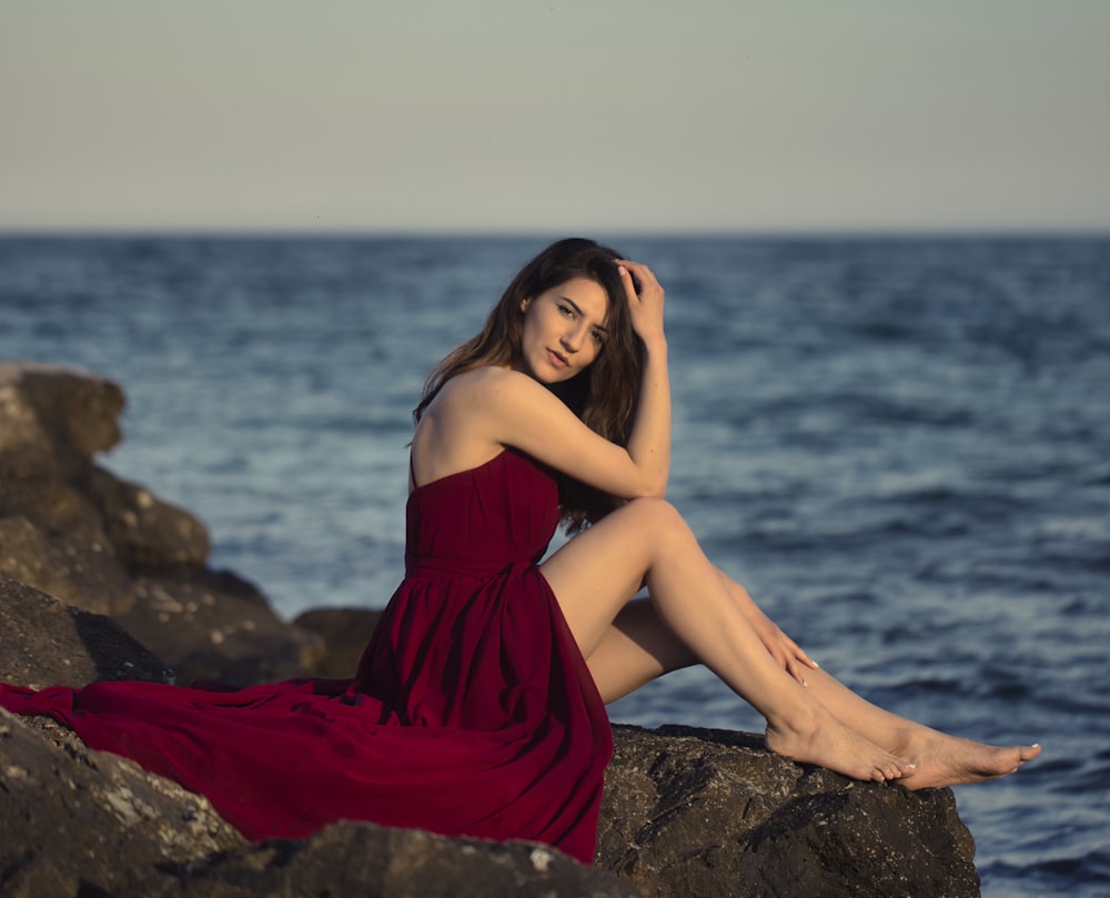 woman in red dress sitting on rock near sea during daytime