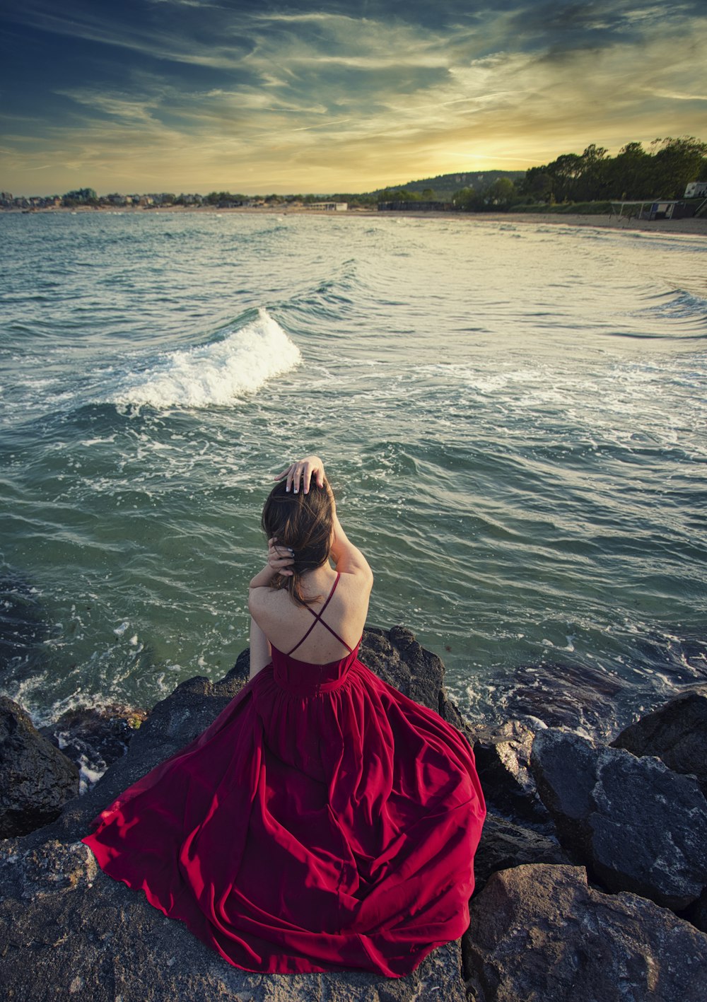 woman in red dress sitting on rock by the sea during daytime
