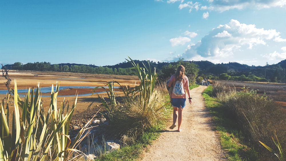 Femme en T-shirt bleu et short marron debout sur un chemin de terre brun pendant la journée
