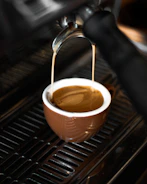 Barista carefully pouring espresso with rich crema into a ceramic cup.