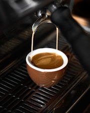 Close-up of a barista pouring rich espresso into a ceramic cup with steam rising.