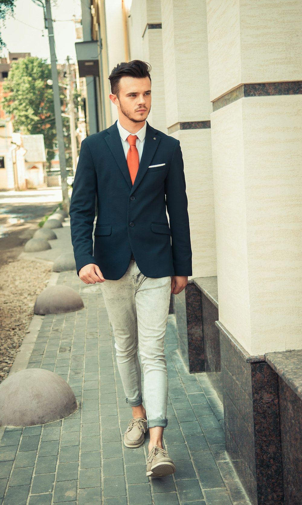 man in blue suit jacket and white pants standing on gray concrete floor