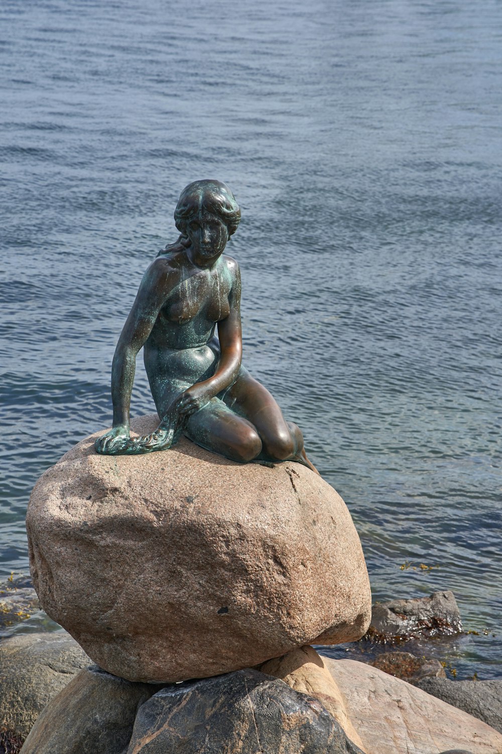 woman sitting on rock statue near body of water during daytime