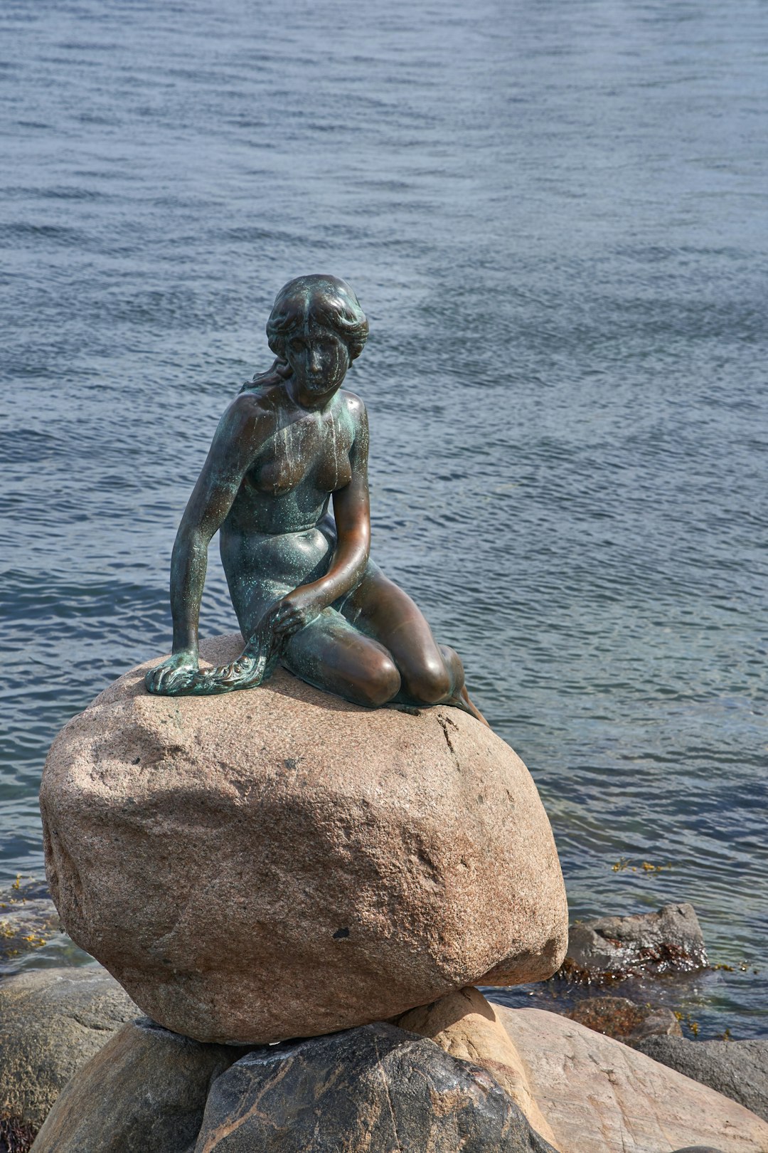 woman sitting on rock statue near body of water during daytime