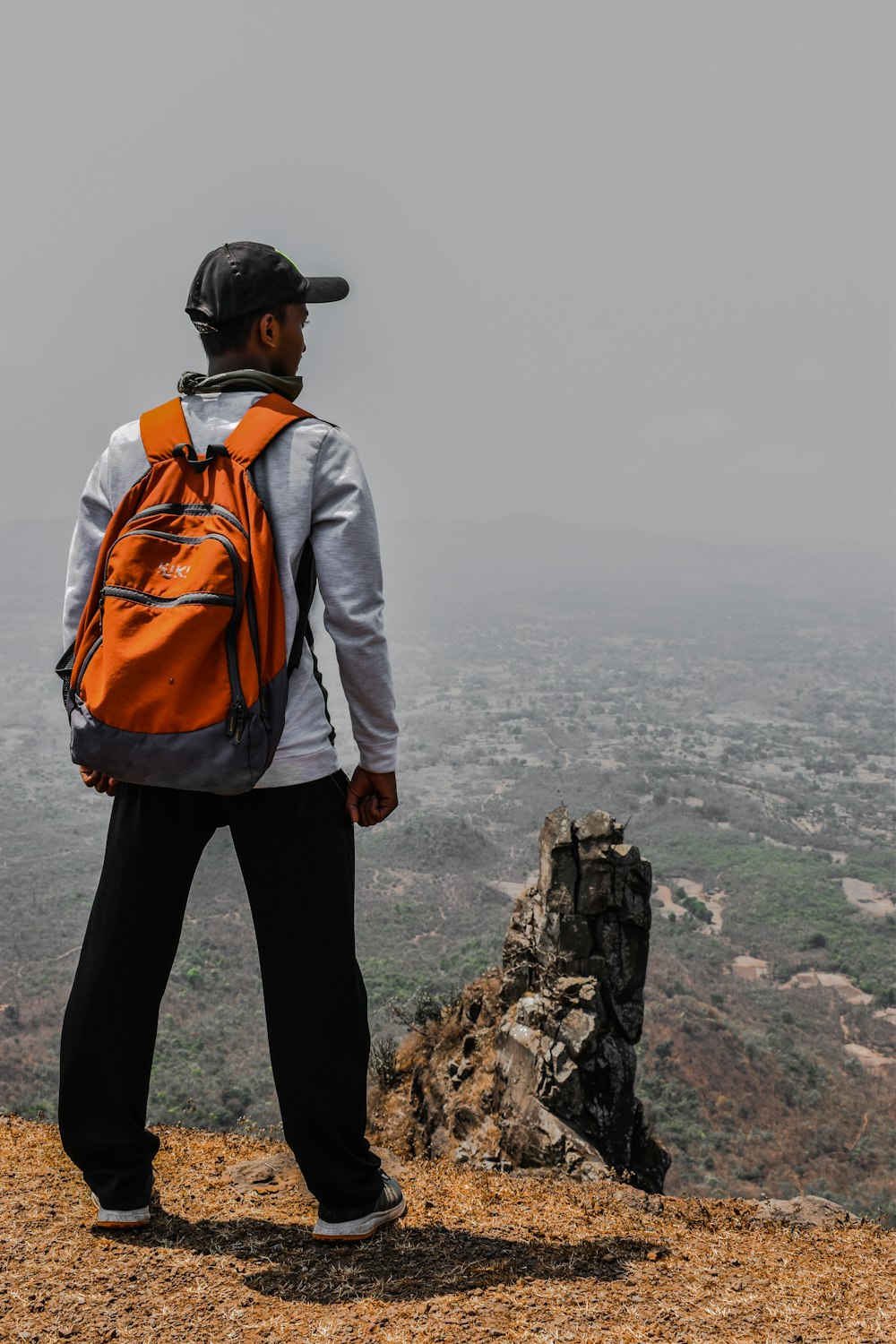 man in gray jacket and orange backpack standing on rock formation during daytime