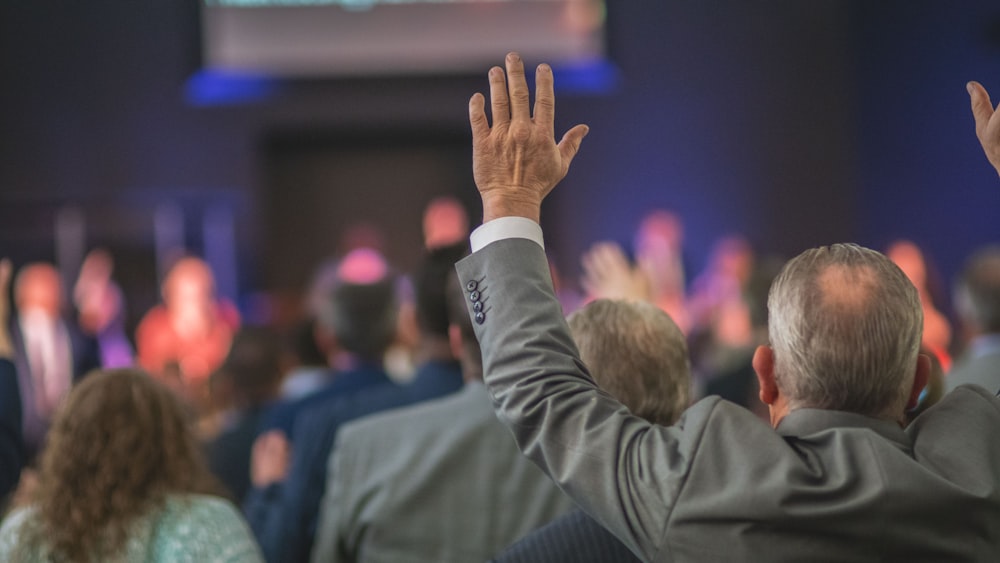 man in black suit jacket raising his right hand