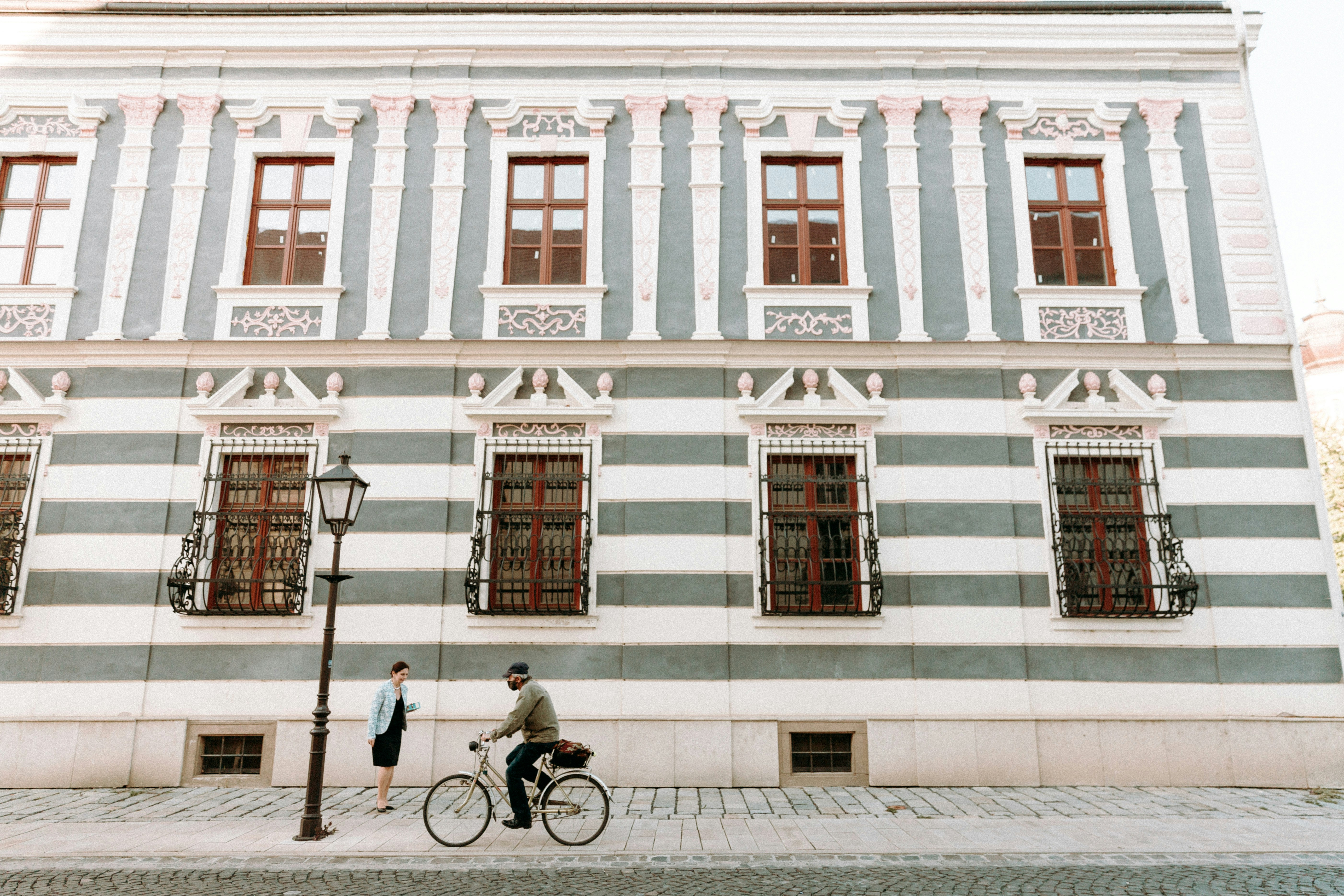 man in black jacket riding bicycle in front of white concrete building during daytime