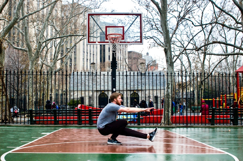 man in blue t-shirt and black pants sitting on basketball hoop