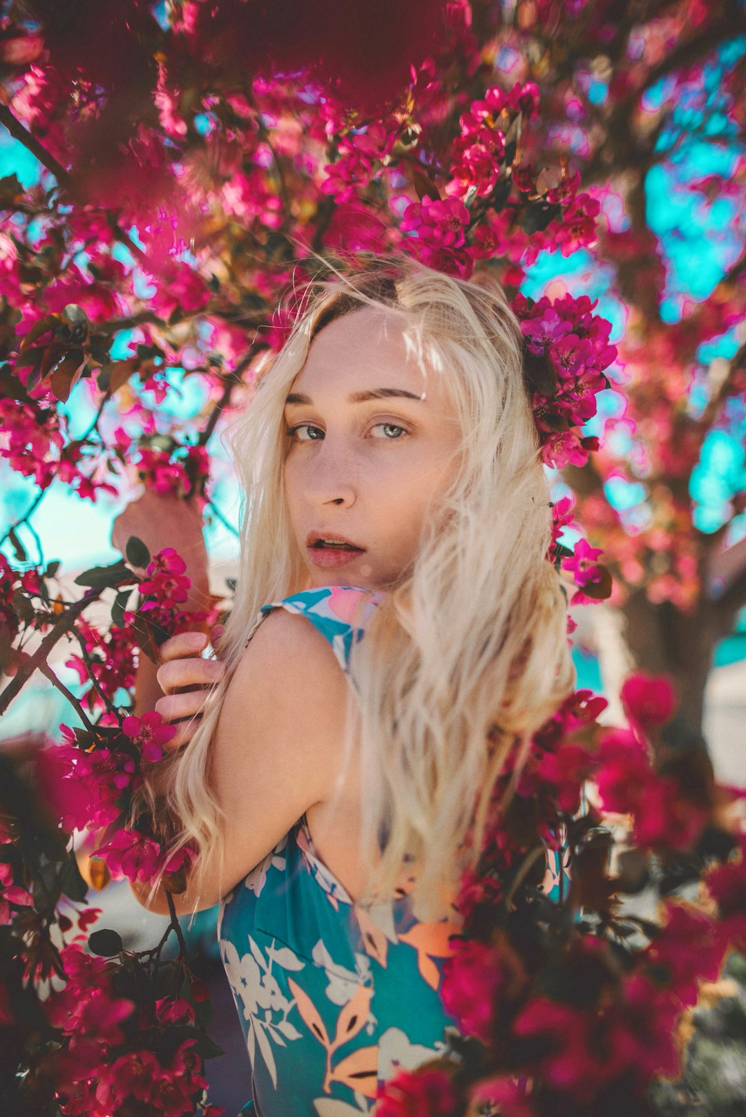 girl in blue tank top standing beside pink flowers