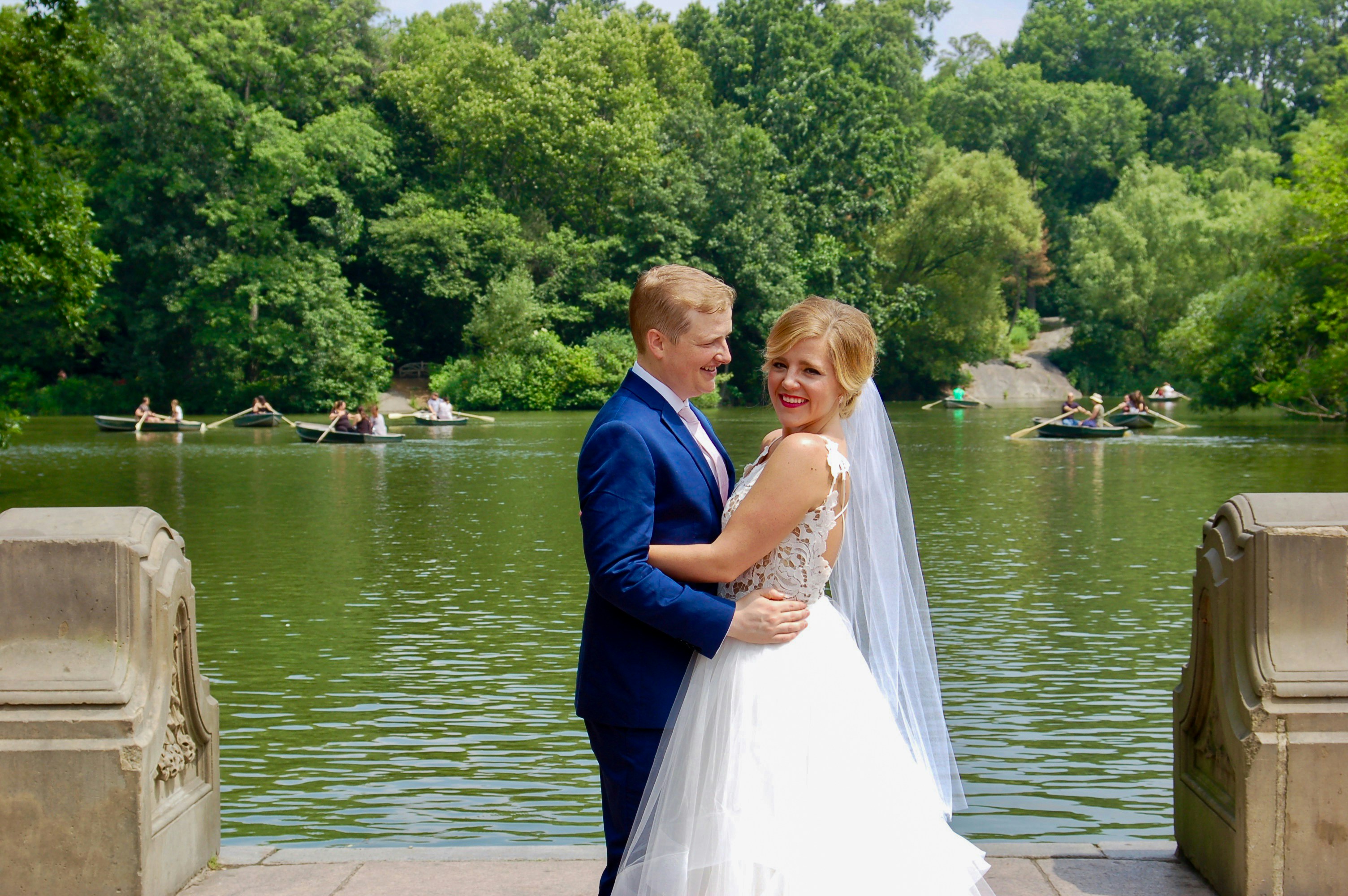 Mann im blauen Anzug und Frau im weißen Brautkleid stehen auf braunem Holzsteg während