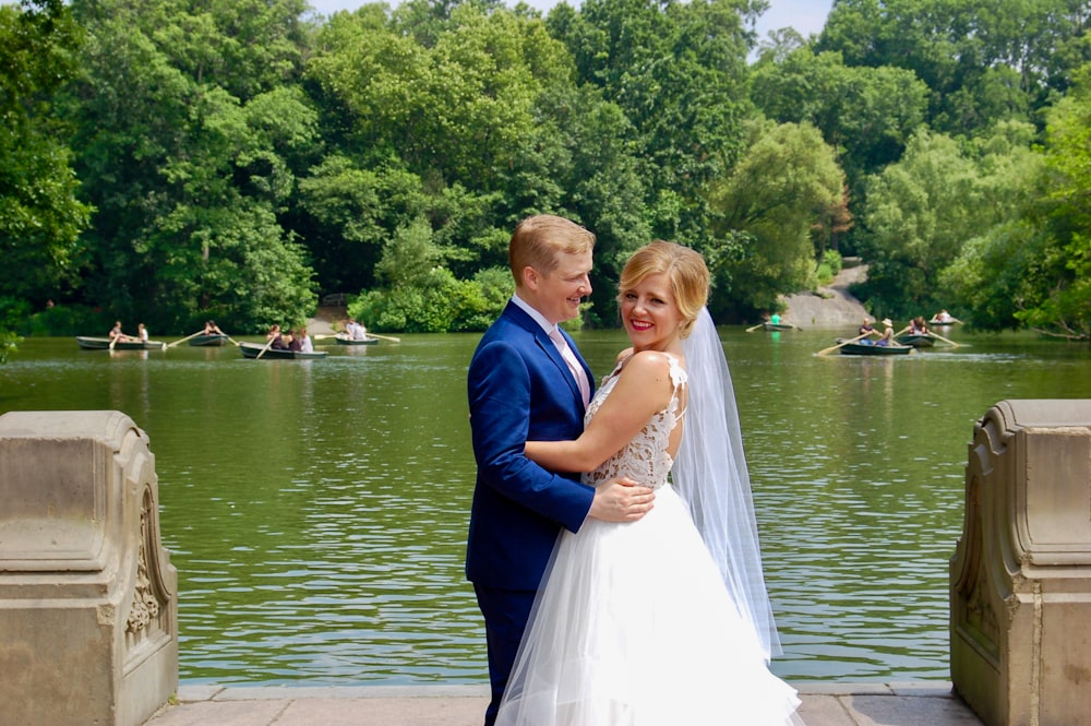 man in blue suit and woman in white wedding dress standing on brown wooden dock during