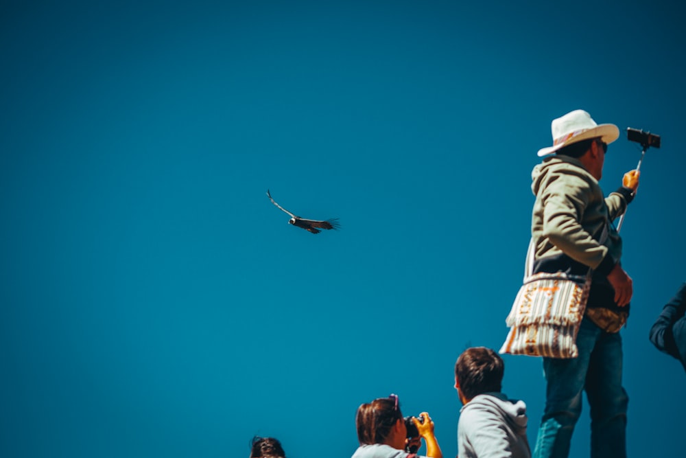 people in white shirt and brown pants with black bird flying in the sky during daytime