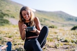 woman in black tank top and black pants sitting on ground holding blue ceramic mug during
