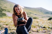woman in black tank top and black pants sitting on ground holding blue ceramic mug during
