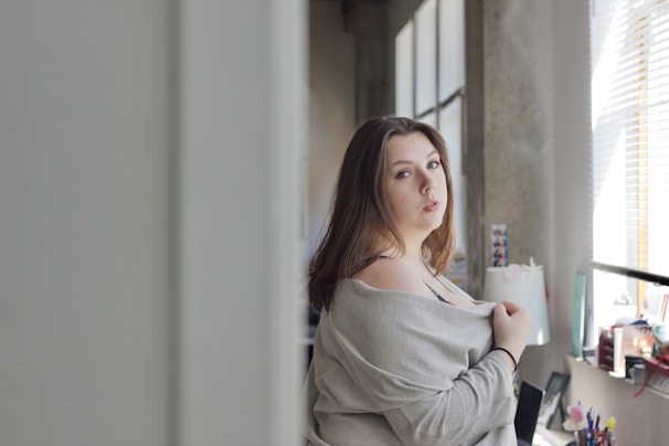 A model wearing a comfy, oversized cardigan standing by a sunlit window.