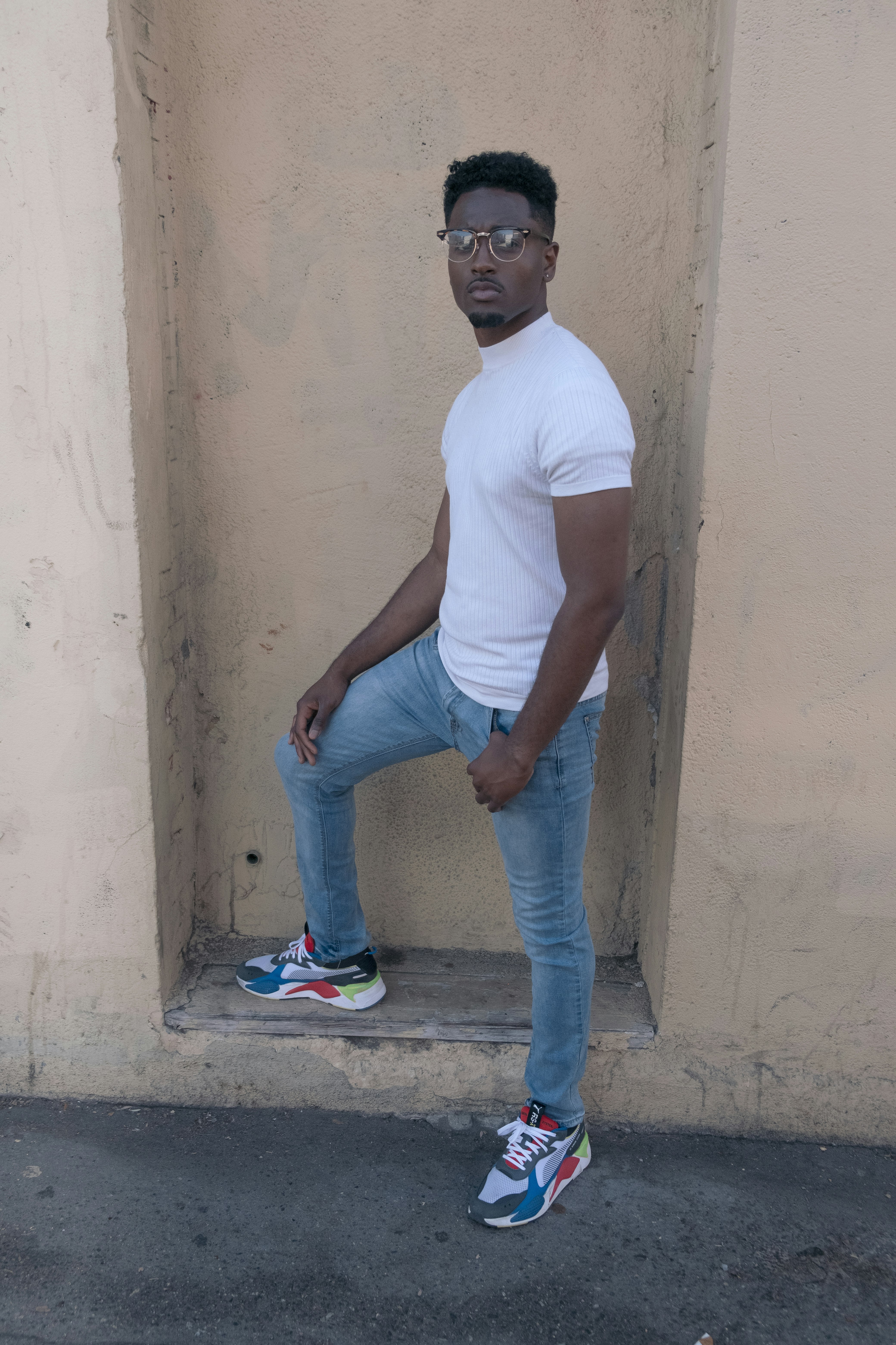 man in white crew neck t-shirt and blue denim jeans standing on gray concrete floor