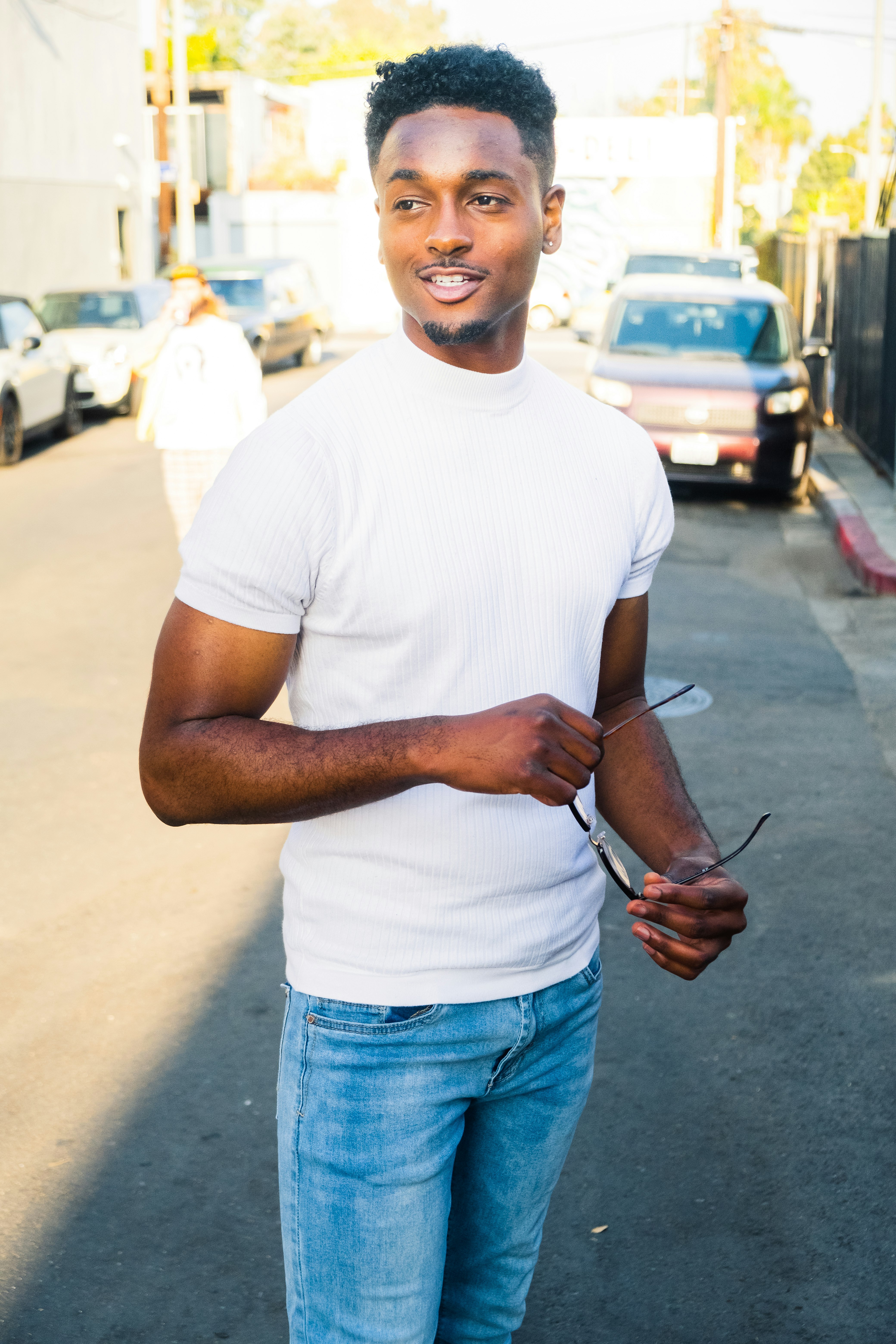 man in white crew neck t-shirt and blue denim jeans standing on sidewalk during daytime