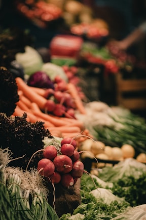A vibrant display of fresh vegetables including radishes, carrots, leafy greens, and other produce neatly arranged. The scene is lively with a focus on natural textures and colors.