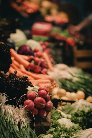 A vibrant display of fresh vegetables including radishes, carrots, leafy greens, and other produce neatly arranged. The scene is lively with a focus on natural textures and colors.