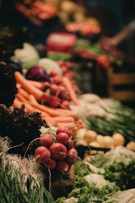 A vibrant display of fresh vegetables including radishes, carrots, leafy greens, and other produce neatly arranged. The scene is lively with a focus on natural textures and colors.