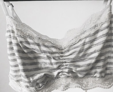 A striped bralette with lace trim, featuring horizontal gray and white lines. The fabric appears soft, and the lace adds a delicate, feminine touch along the top and bottom edges.