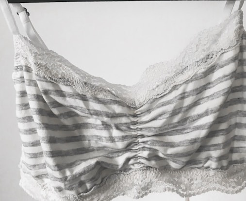 A striped bralette with lace trim, featuring horizontal gray and white lines. The fabric appears soft, and the lace adds a delicate, feminine touch along the top and bottom edges.