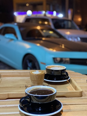 A steaming cup of artisan coffee resting on a wooden table beside a shiny, freshly detailed car.