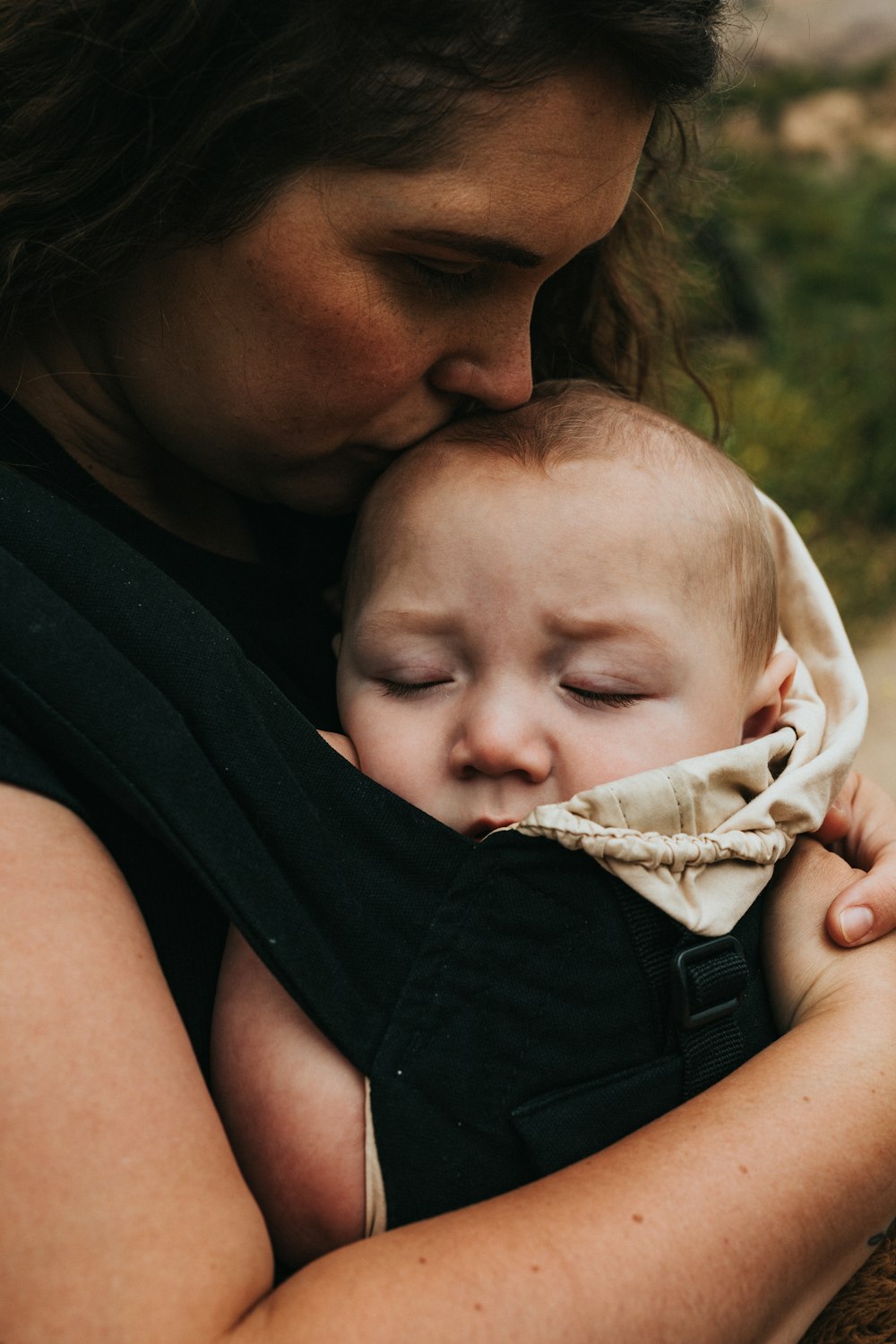 woman in black sleeveless shirt carrying baby in white onesie