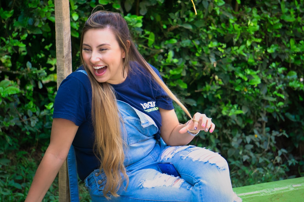 girl in blue t-shirt and blue denim jeans sitting on brown wooden bench