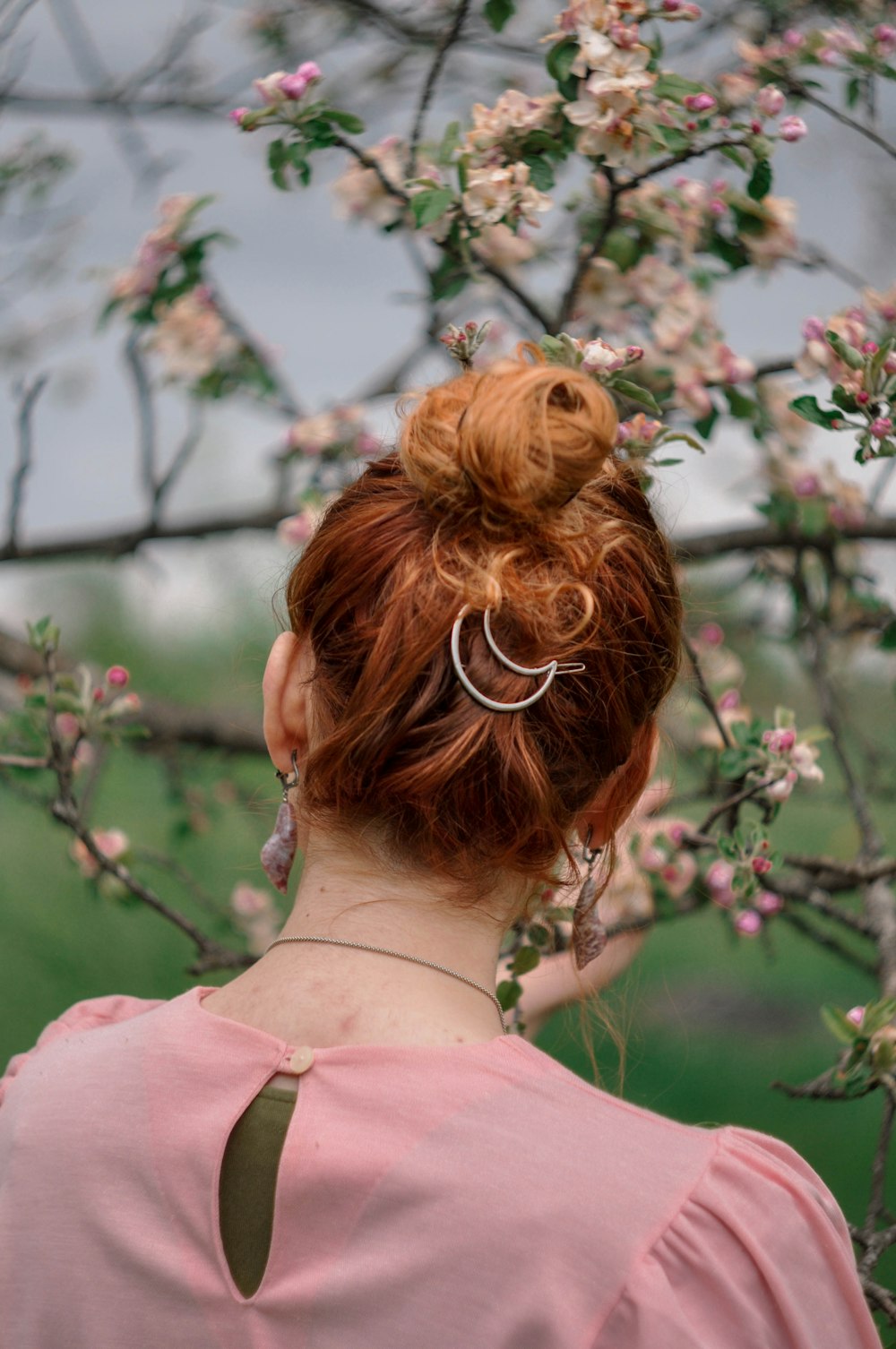 woman in pink shirt with brown hair under white and pink cherry blossom tree during daytime