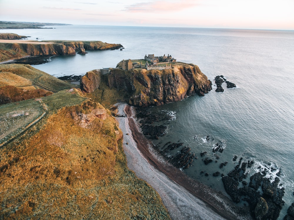 brown and green cliff beside body of water during daytime