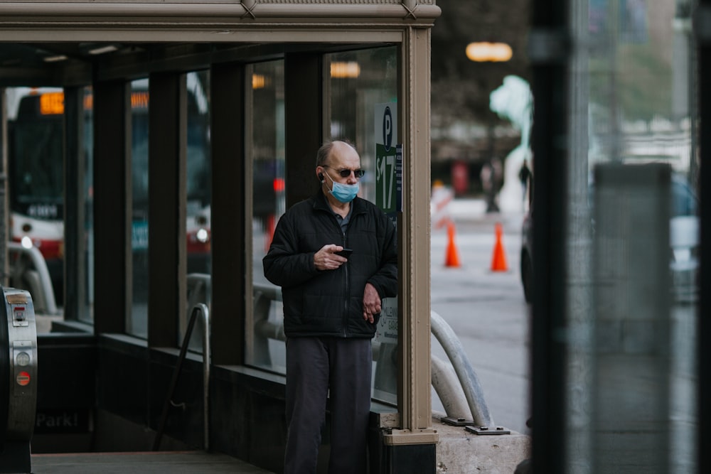 homme en veste de costume noire et pantalon noir debout à côté d’une fenêtre en verre